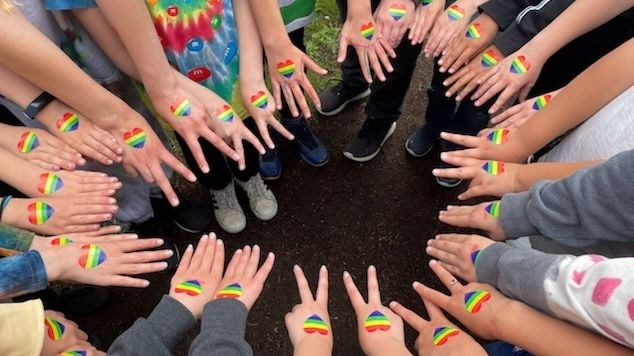 Students with their hands in a circle wearing rainbow heart stickers for Pride Month.
